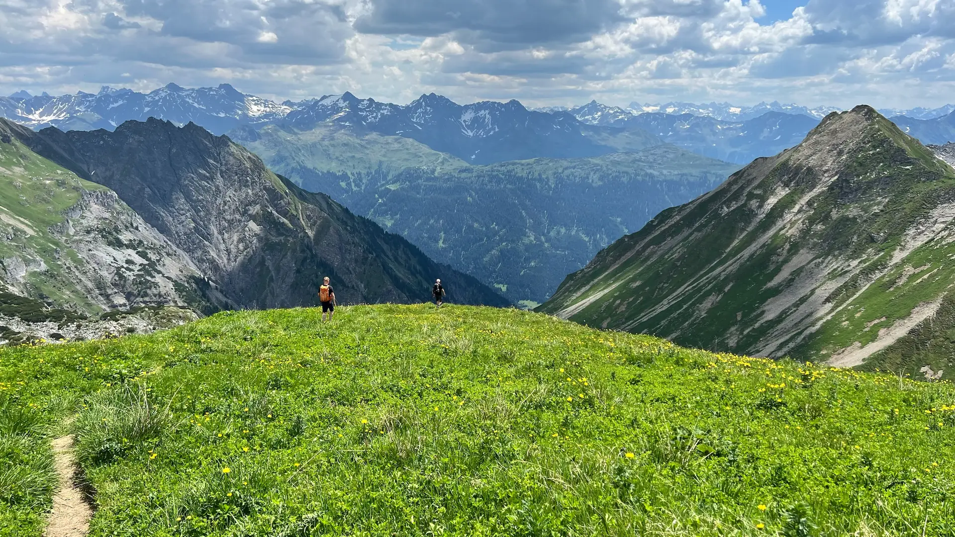 Zwei Wandernde vor einem weiten Bergpanorama